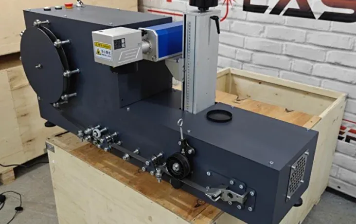 An assembled marking machine on a pallet before shipping: laser head on its column and the tape feed unit
