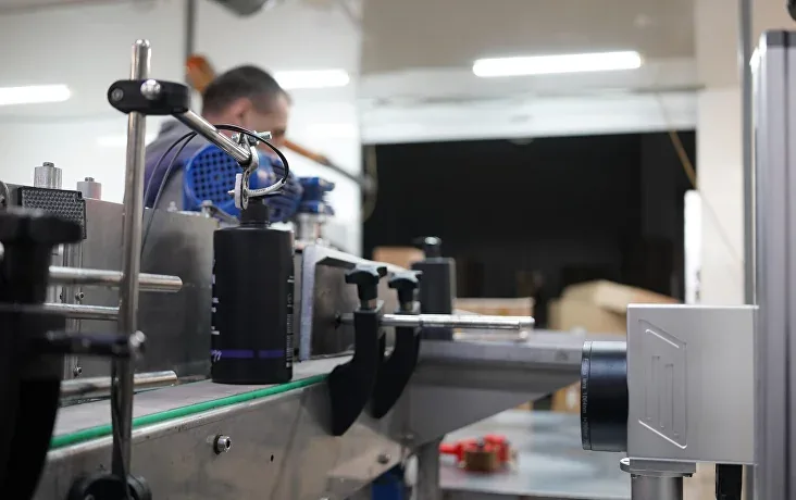 Laser marker on a bracket above a conveyor of household-chemical bottles, code inspection camera on the right