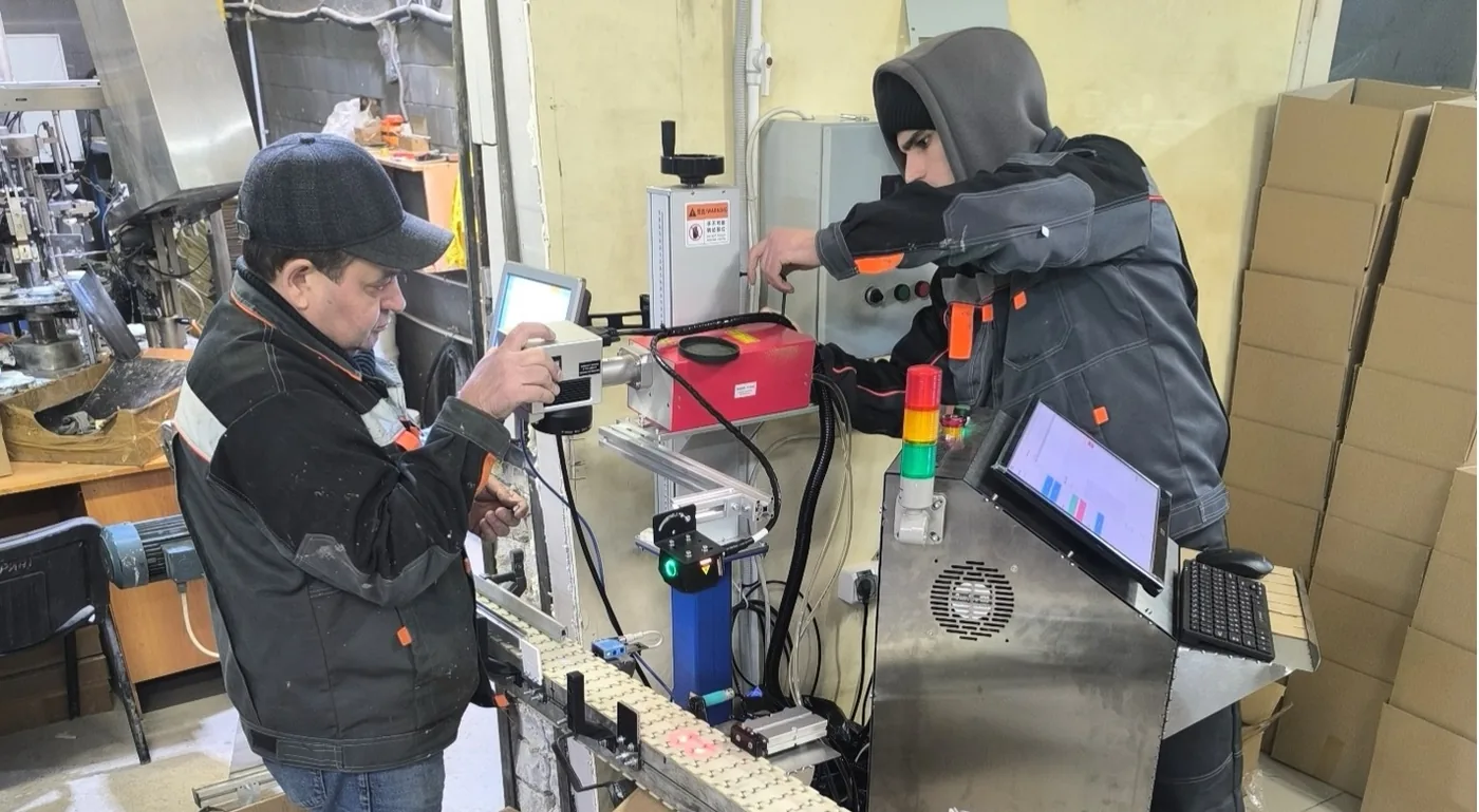 Commissioning a station on a sealant-tube line: laser marker, camera illumination above the chain conveyor and a stand with the operator screen