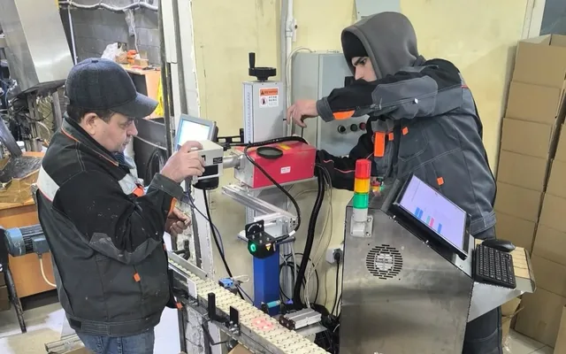 Two commissioning engineers at a sealant-tube line: laser marker, signal tower and the operator screen