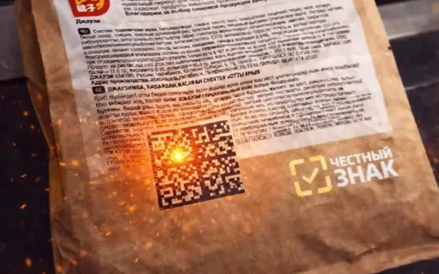 A laser applying DataMatrix to a kraft flexible-packaging bag — sparks and the Chestny Znak sign in frame