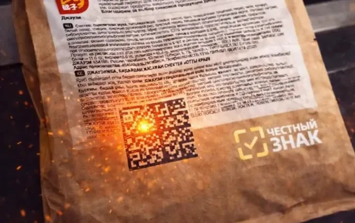 A frame from the line: a laser applying DataMatrix to a kraft flexible-packaging bag, sparks and the Chestny Znak sign in shot